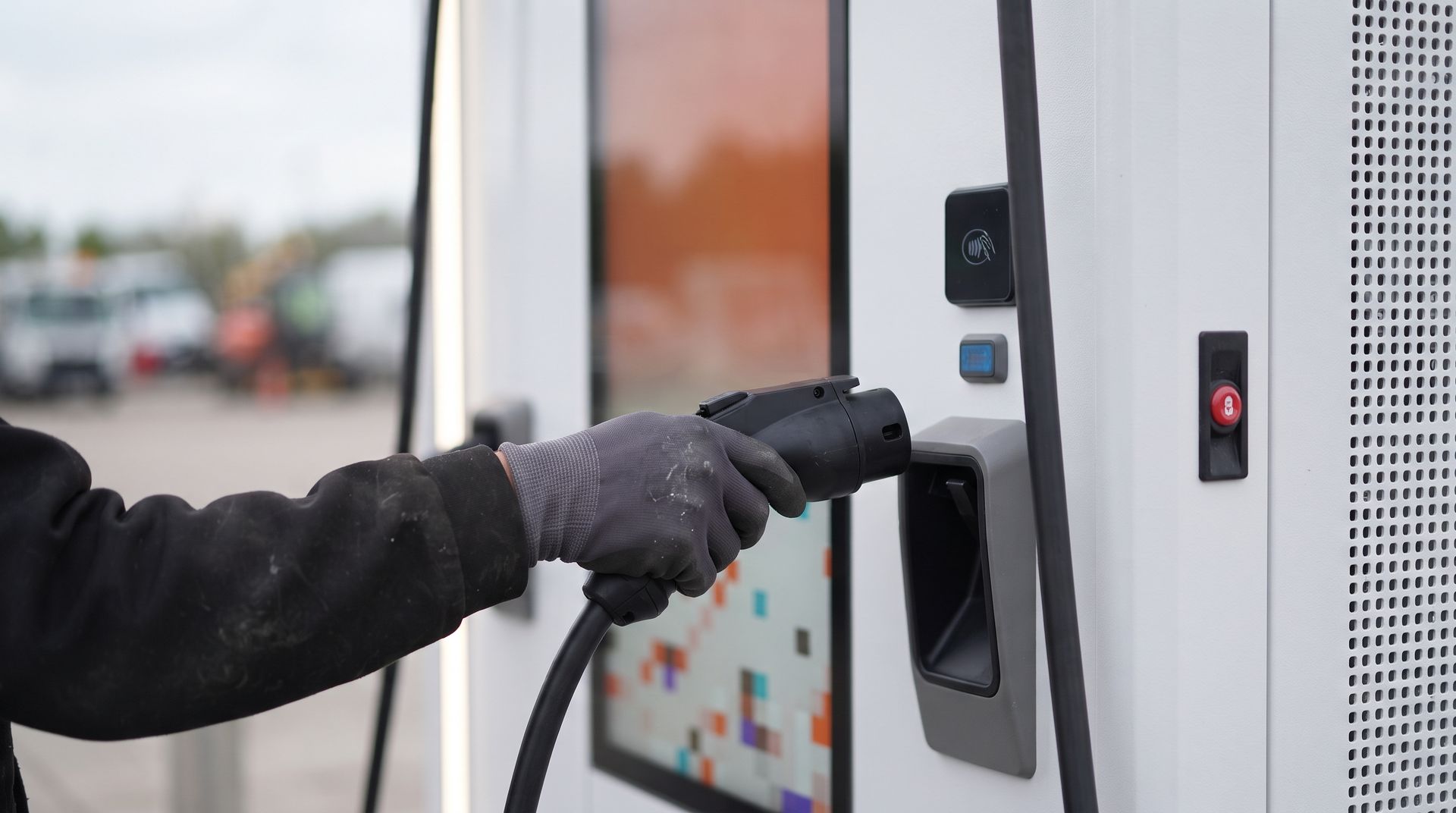 A gloved hand lifting a CCS2 connector from an Allye MEV charger